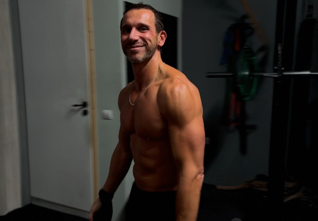 Yorgos standing amidst a dark background with his shirt off.